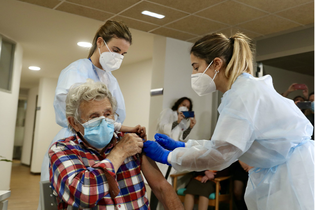 An elderly woman wearing a blue mask received a vaccine from two nurses wearing personal protective equipment