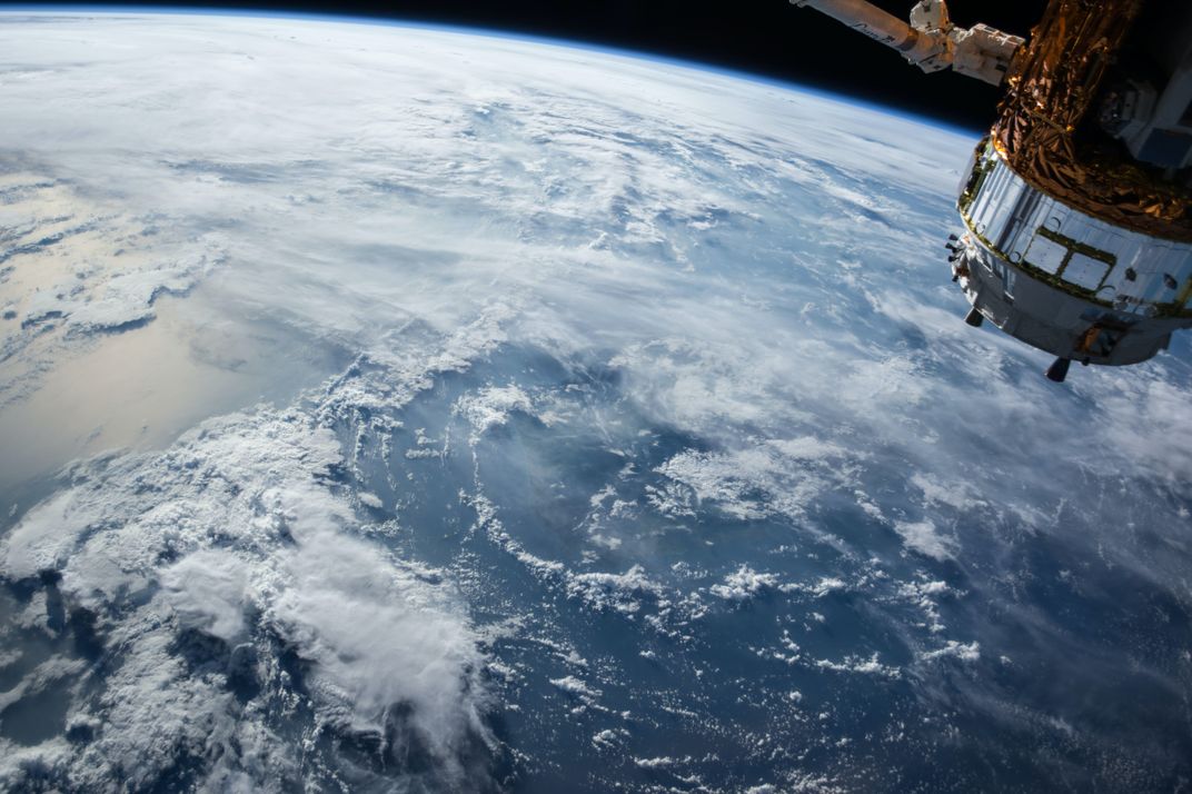 A satellite hovers over a cloudy view of our planet.