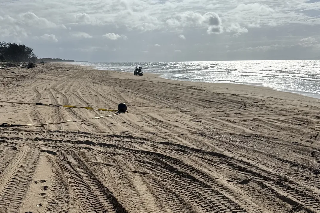 a ball on a beach with a vehicle in the background