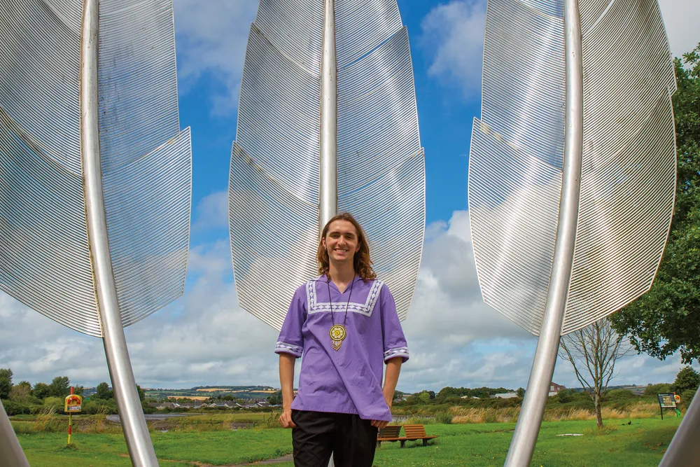 a man in purple shirt stands in front of a steel monument