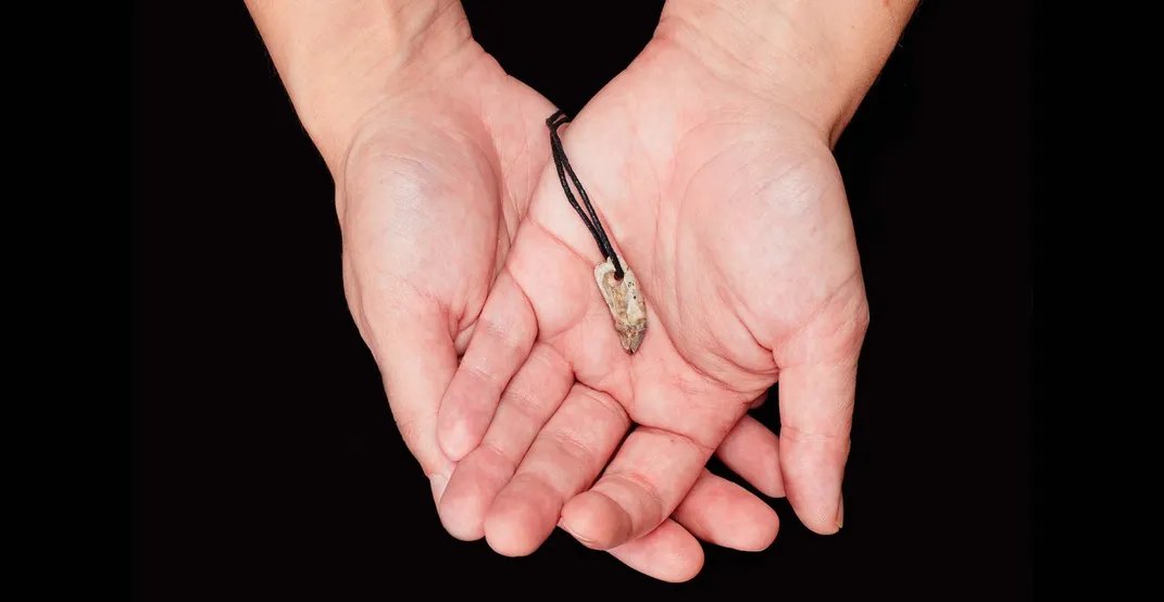 A person's upturned hands holding a tooth pendant