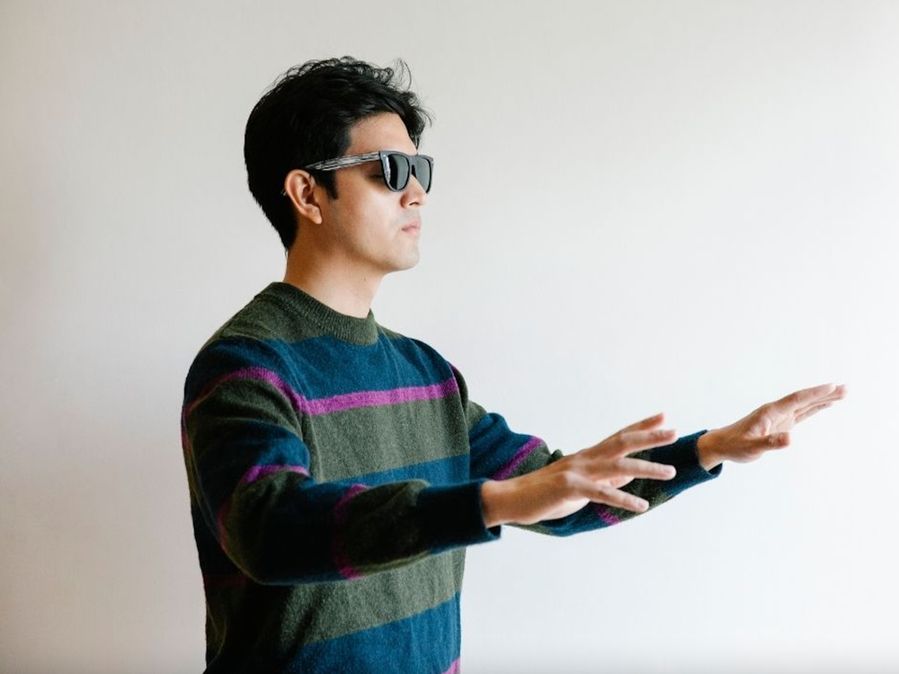 A man wearing sunglasses holds his arms up and in front of him 