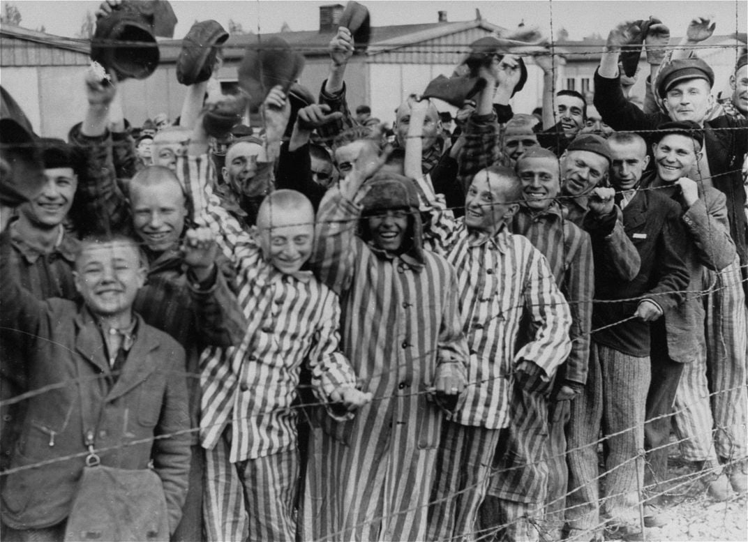 Prisoners at Dachau greet their Allied liberators from behind a barbed-wire fence.