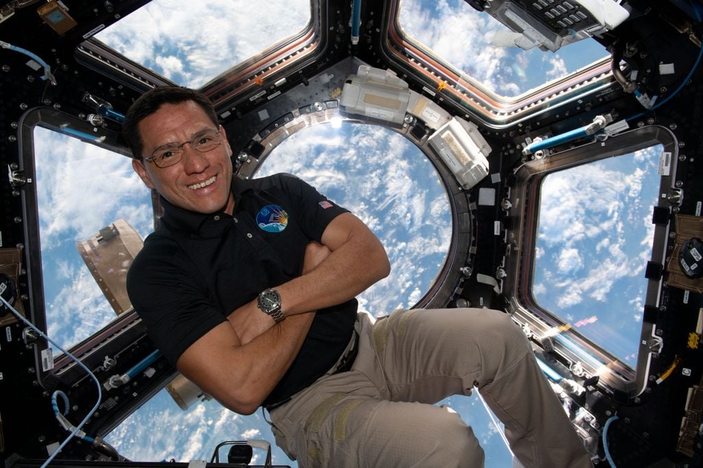 Frank Rubio floats with his arms crossed on the International Space Station with a view of Earth out a window behind him