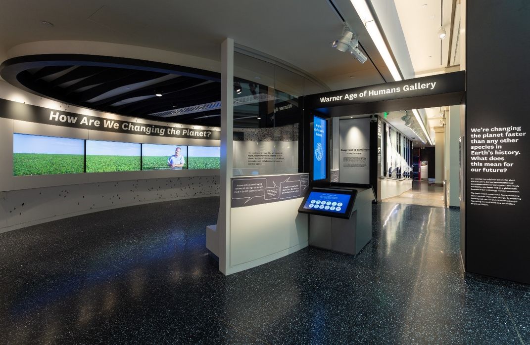 Small theater featuring four screens and "How Are We Changing the Planet?" in white on a black wall at the Smithsonian's National Museum of Natural History