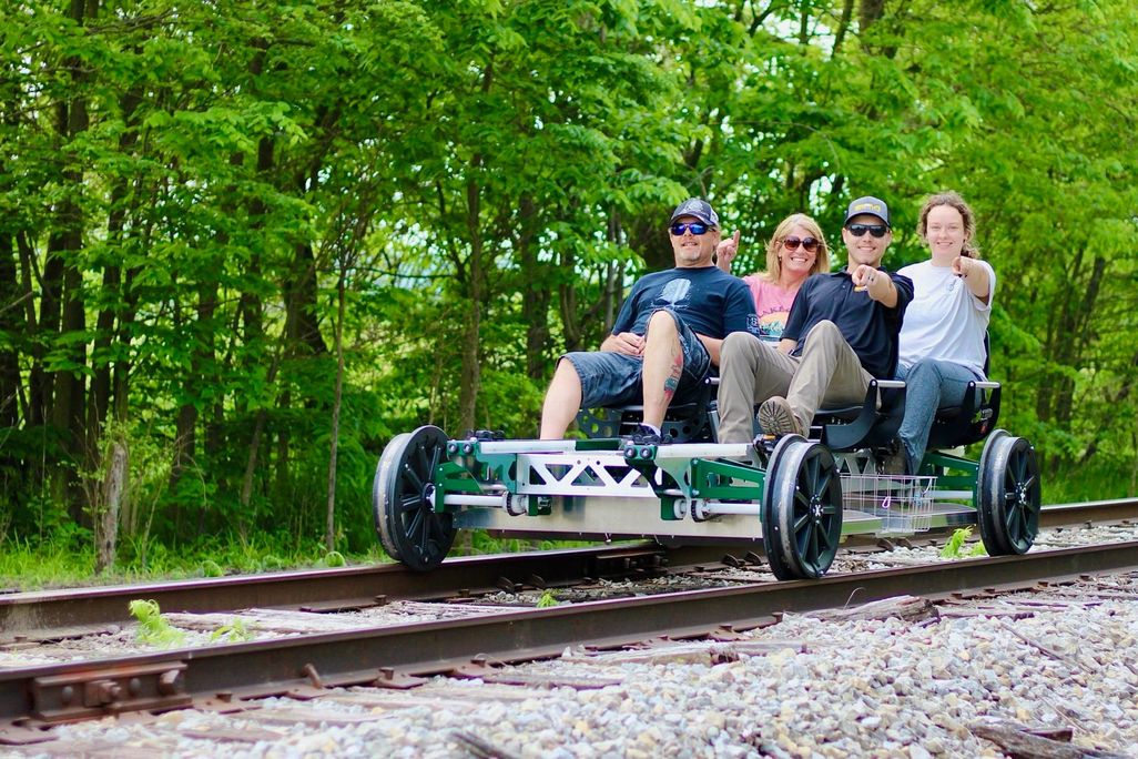 Group of four people riding a railbike while pointing at the camera and smiling