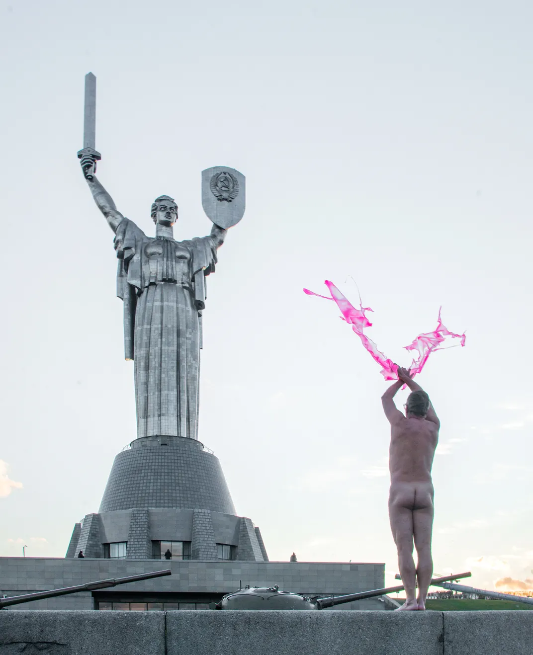 man standing nude facing monument tossing paint toward the statue