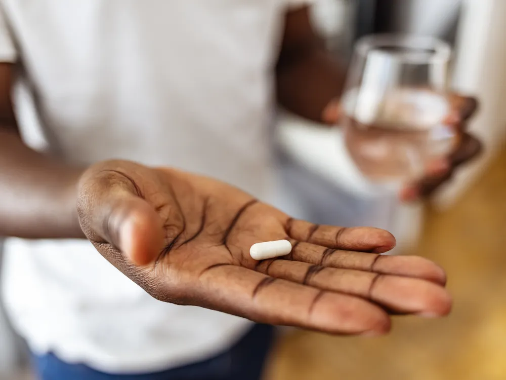 A man holding a white capsule pill and a glass of water