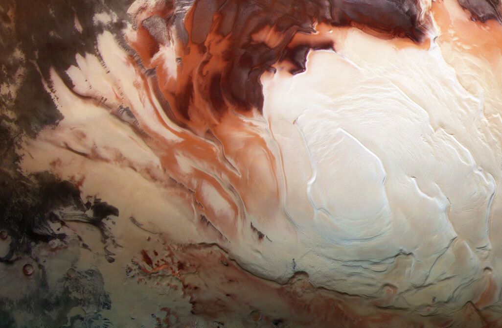 An image of Mars's South Pole. The photo shows a white icy cap surrounded by swirls of various shades of red. 