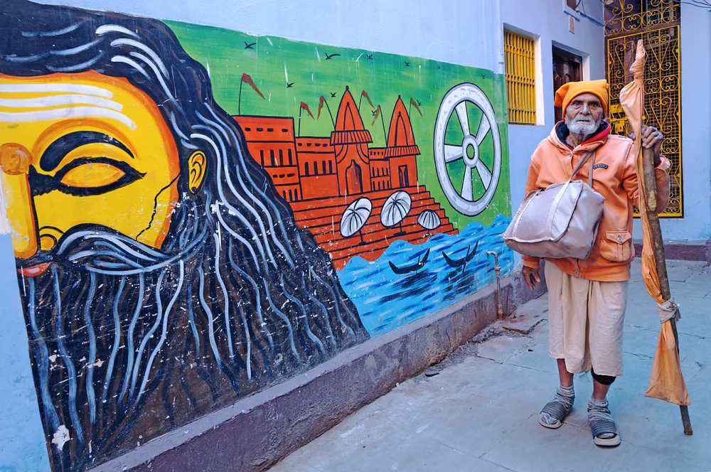An old man is moving alone by a wonderful wall where images of the God of Hindu Mythology have been painted.