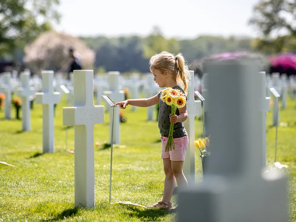 A child places flower on a grave at the Netherlands American Cemetery