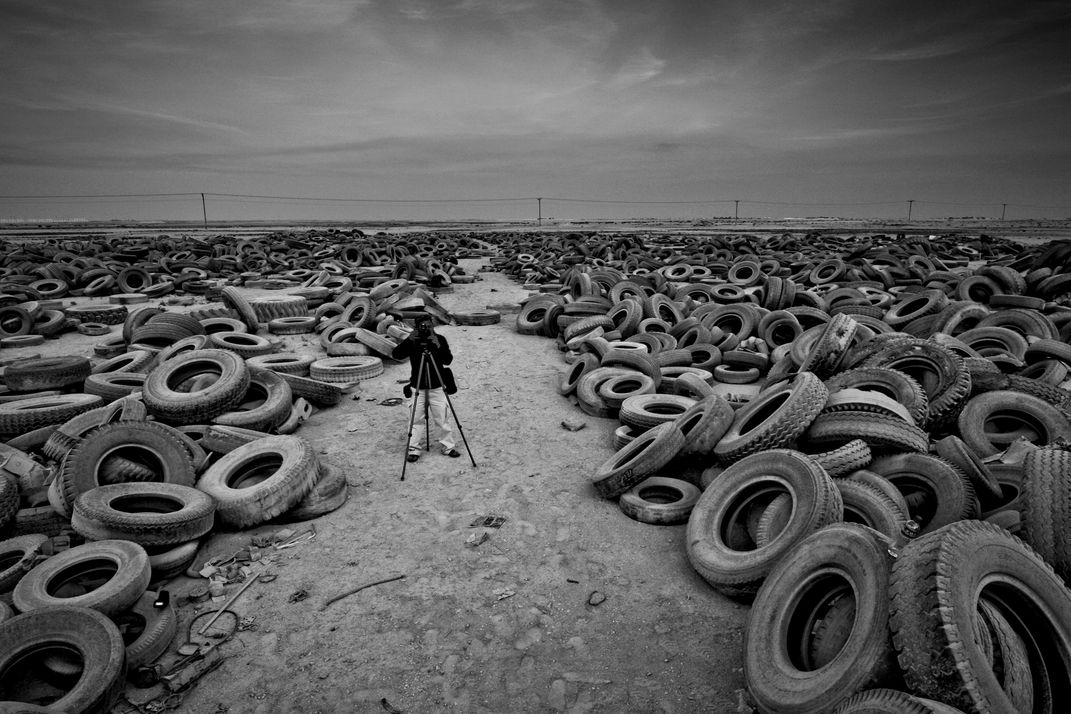 A photographer taking photos of a junkyard of broken tires placed