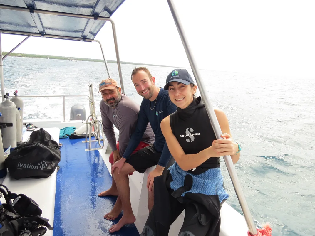 Three scientists sit on boat with grey sky in background
