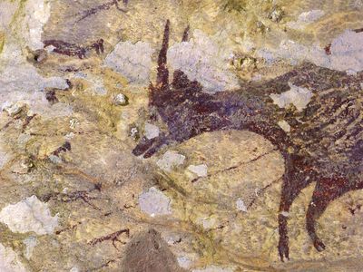 Six humanoid figures with animal features surround an anoa, a small type of buffalo, in a 44,000-year-old Indonesian cave mural.
