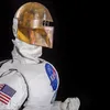 Photographed against a black background is a robot in profile wearing a silver uniform and golden-colored helmet.
