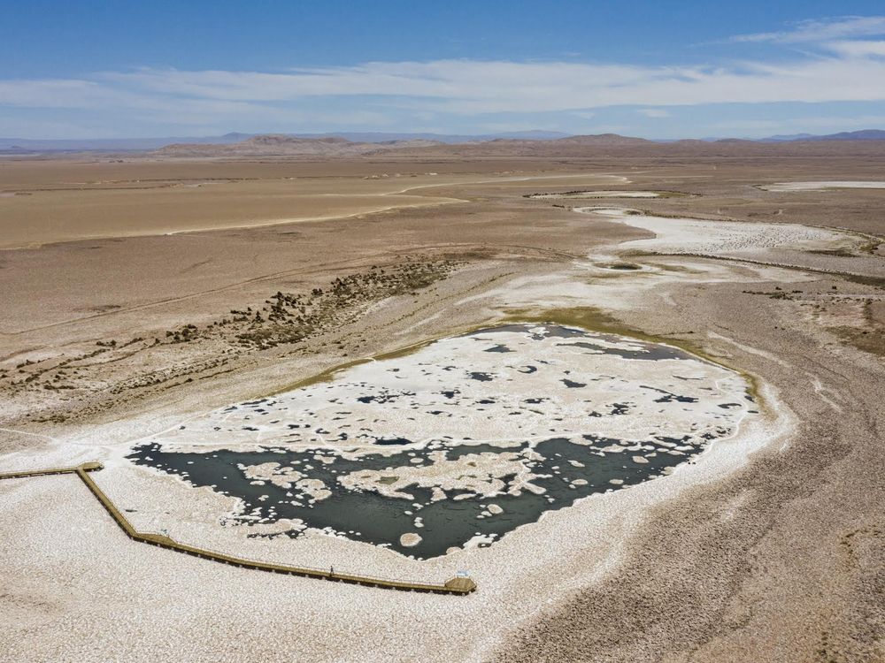 In an aerial shot of the desert, a dry lakebed is surrounded by swaths of white salt flats.