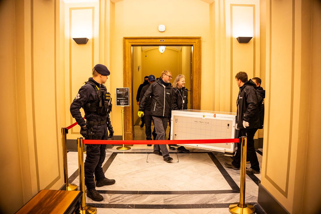 people carry a box out of a hallway with security around them
