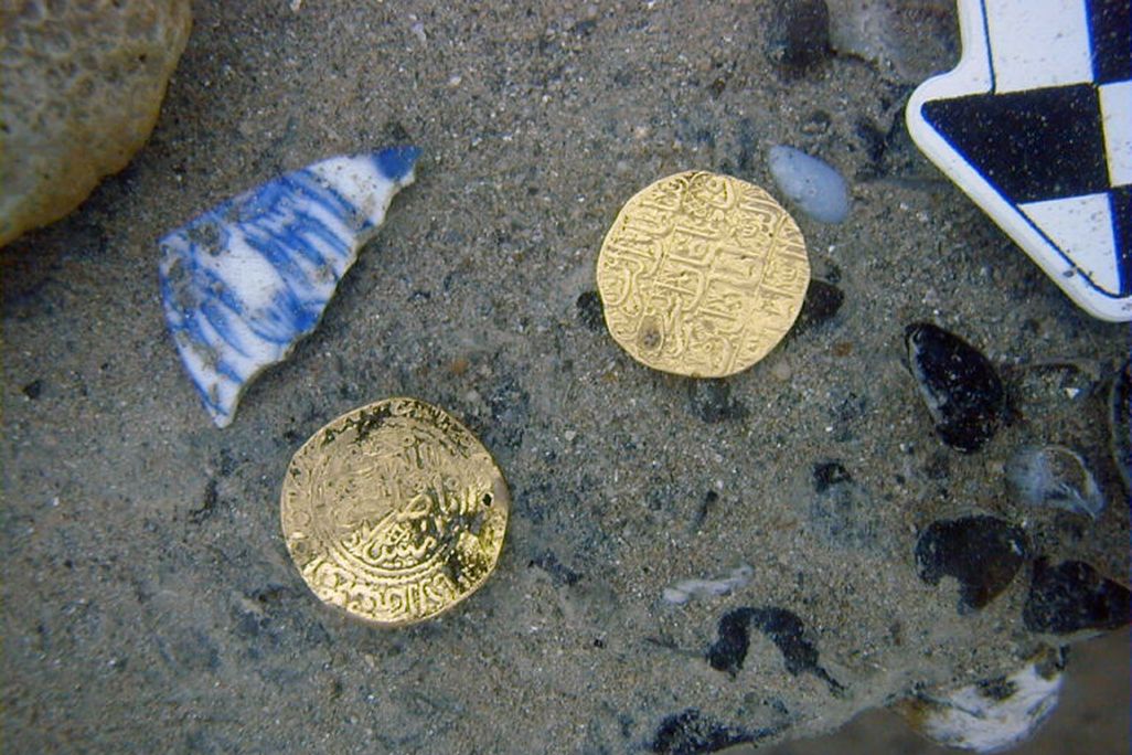 Two gold coins and bit of blue pottery resting on sand