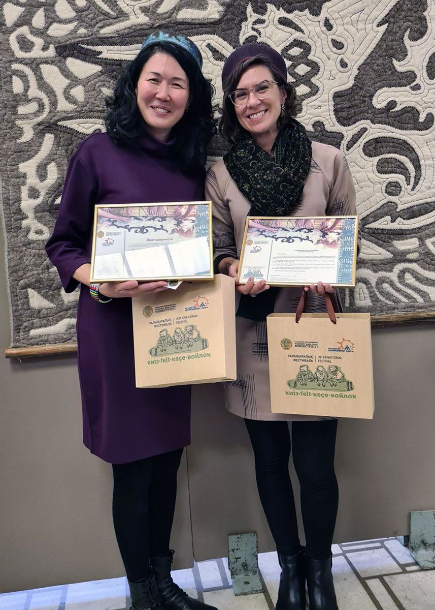 Two women poses, each holding a plaque and a tote bag.