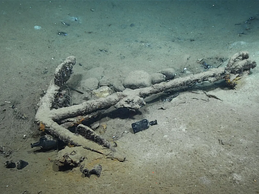 An anchor surrounded by bottles and other debris, covered in ocean sand and muck