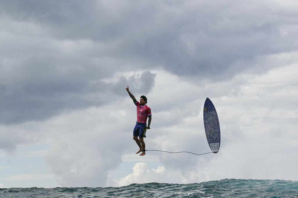 Surfer and his surfboard floating through the air above ocean water