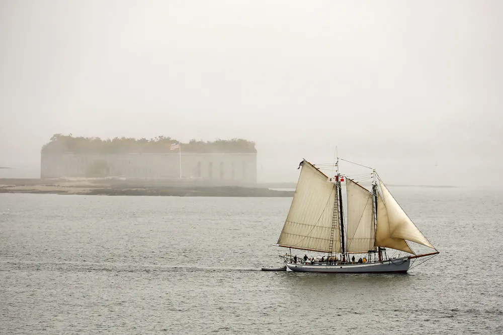 OPENER - Flying Maine’s original state flag, from 1901, the schooner Timberwind sails out of the fog, past Fort Gorges in Casco Bay.