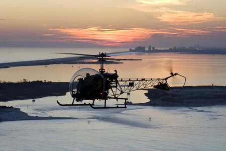 The trademark plexiglass sphere enclosing its cockpit gave the Bell 47 its nickname and provides the pilot cruising this beach a glorious view of a Florida sunset.