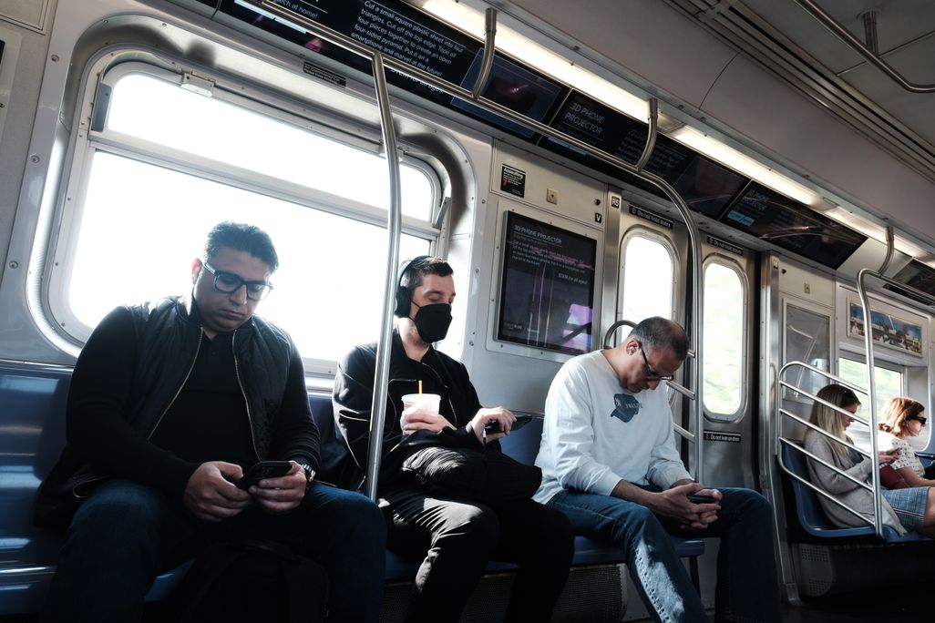 People sitting on a train, one with a mask on