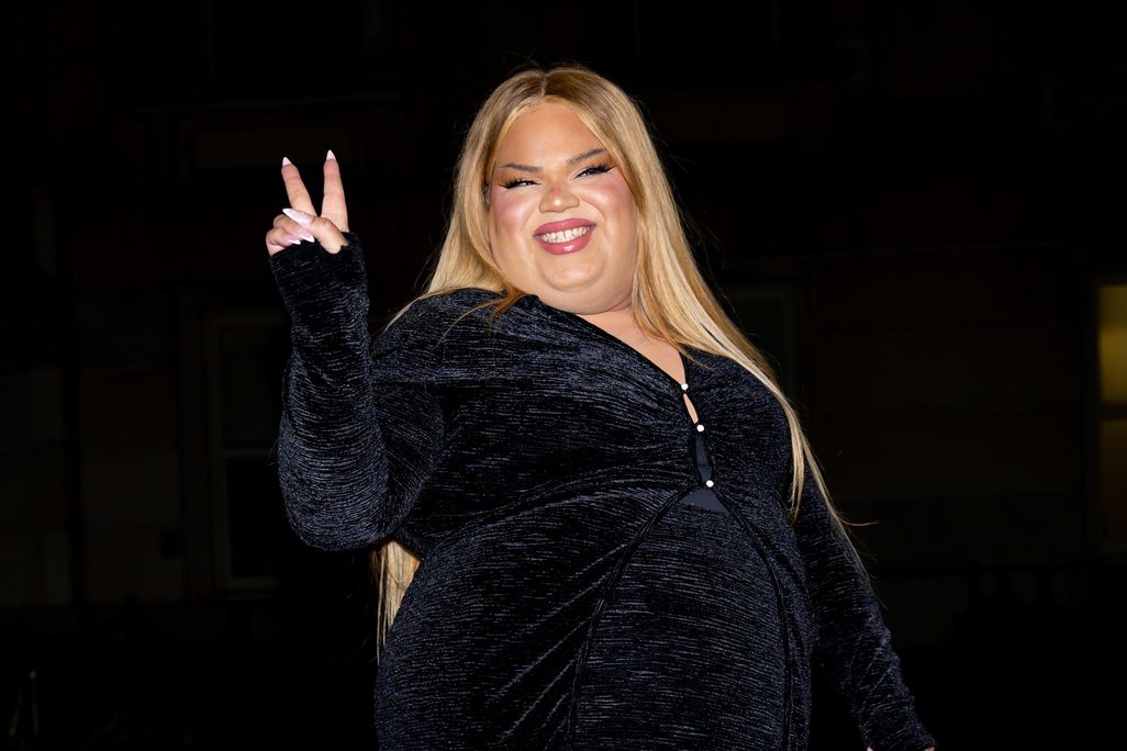 Woman with blond hair wearing black and holding up one hand with a peace sign