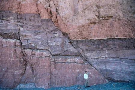 A person stands in front of a fault in Utah. Better understanding how rocks behave under stress and along faults like this could help geologists more accurately identify places at risk of earthquakes.
