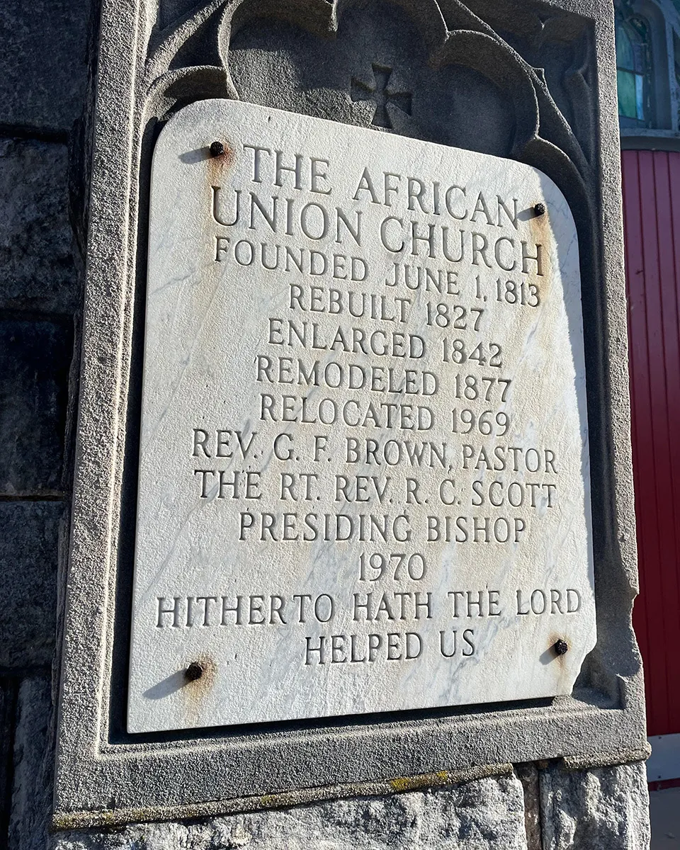 Etched stone plaque with an equilateral cross above. Text on the plaque:  The African Union Church. Founded June 1, 1813. Rebuilt 1827. Enlarged 1842. Remodeled 1877. Relocated 1969. Rev. G. F. Brown, Pastor. The Rt. Rev. R. C. Scott, Presiding Bishop. 19