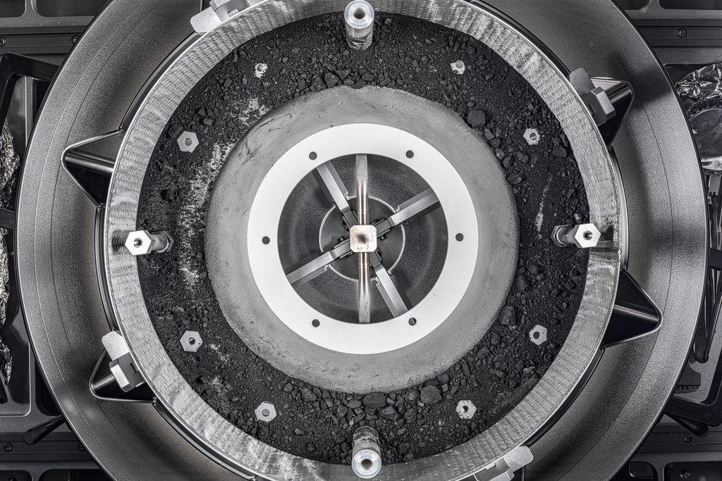 An aerial view of an open circular and grey canister with bits of dust and tiny rocks inside