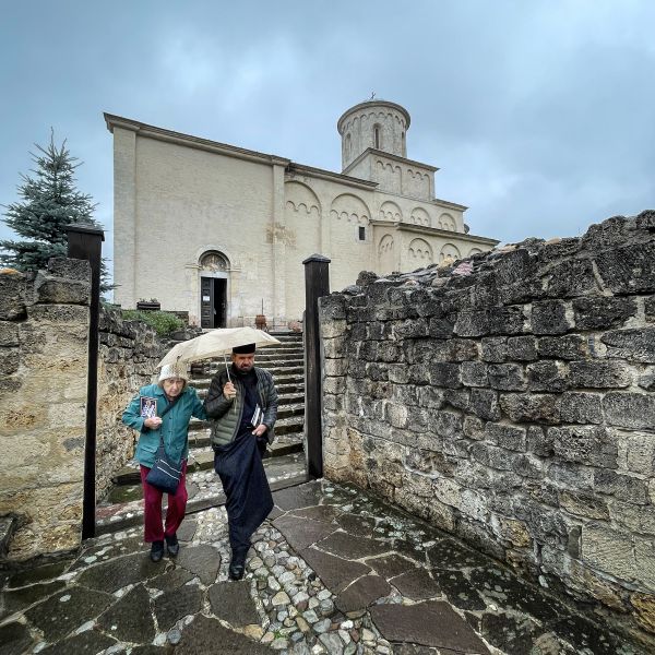 Fr. Blasko and Marie walk slowy from the church in the rain thumbnail