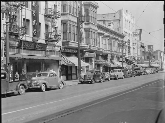 Street scene in black and white with store fronts of buildings, cars, Japanese lettering on one building