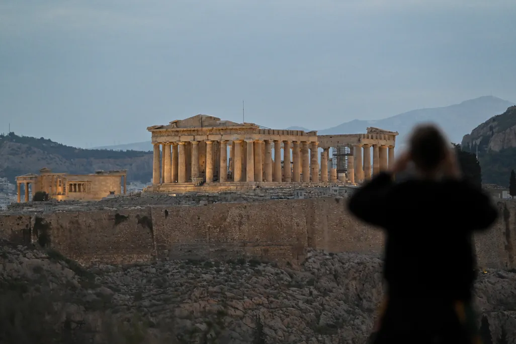 Back of a woman taking a photo of the Parthenon at dusk