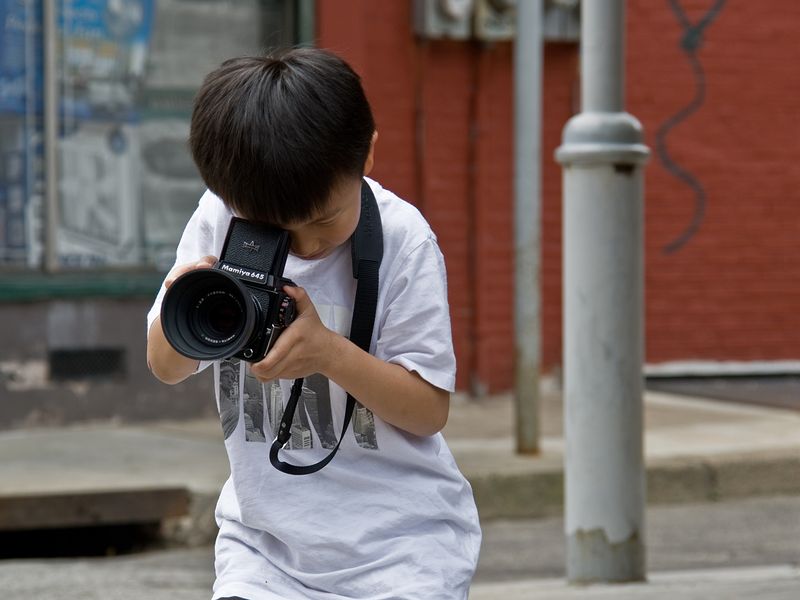 asian-boy-in-italian-market-philadelphia-playing-with-a-mamiya-camera