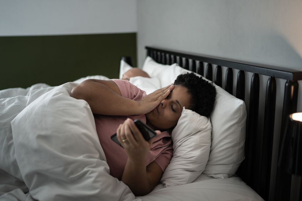 A woman lays in bed and looks at her phone