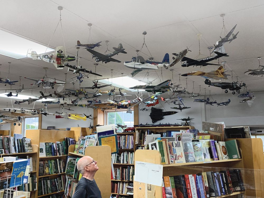 man looking up at model planes above bookshop shelves