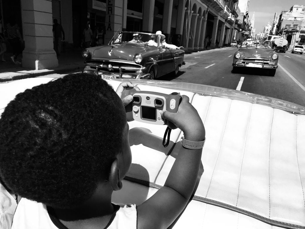 12 - A budding photographer recognizes a scene worth capturing as two classic cars move into the frame.