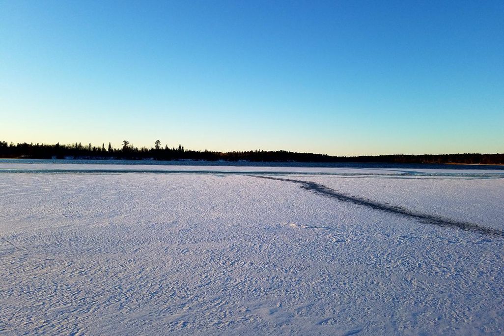 A photograph of a frozen lake landscape with trees on the distant horizon