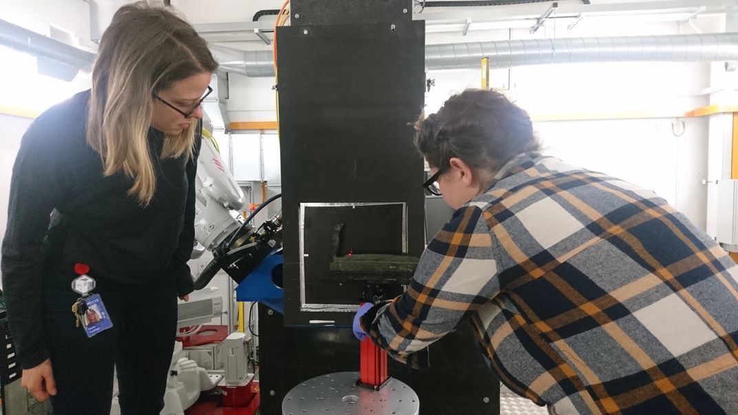 Two women analyzing a small coffin in a lab