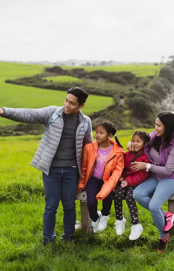 Portrait of a family (a man, a woman and two girls) standing alone in a grassy landscape and pointing while looking off to the left of the frame.