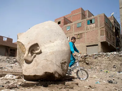 A boy rides his bike by the recently discovered statue that may be of Pharaoh Ramses II, one of the Egypt's most famous ancient rulers.