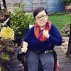 Stacey Park Milbern seated in a power chair in a lush green background with flowers and succulents surrounding her.