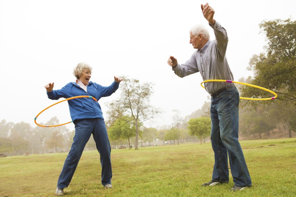 an older woman and older man hula hooping in a park and smiling