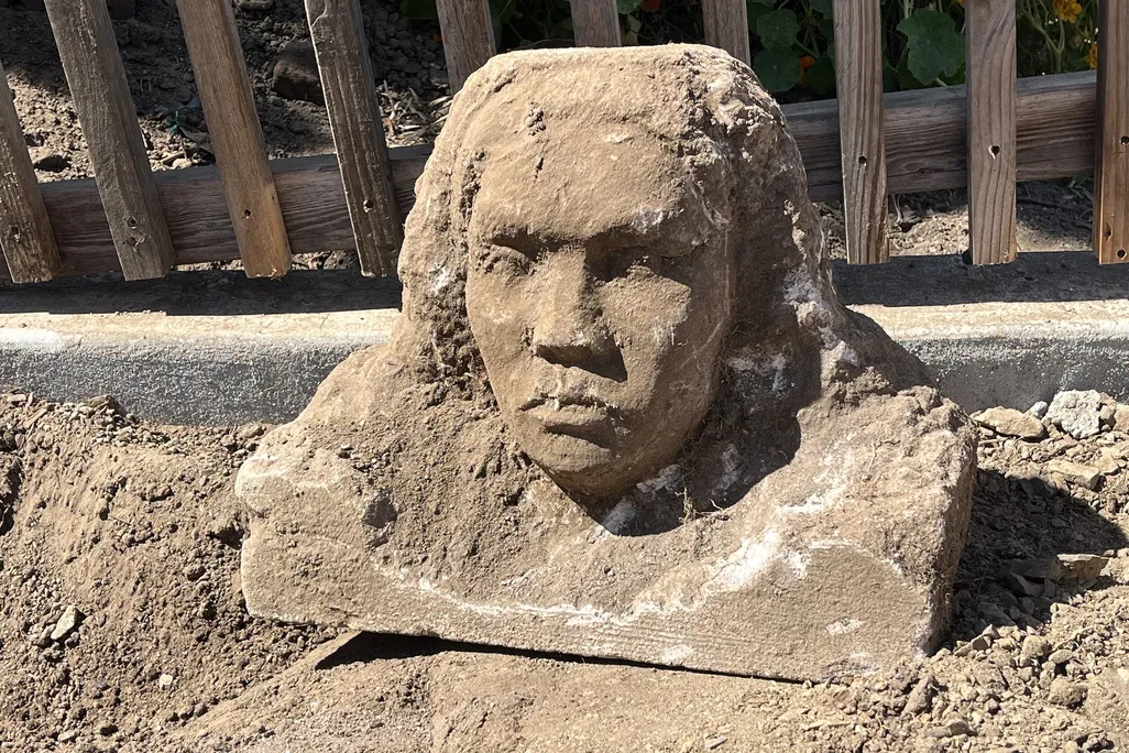 A dirt-covered bust of a woman sitting next to a fence on the ground