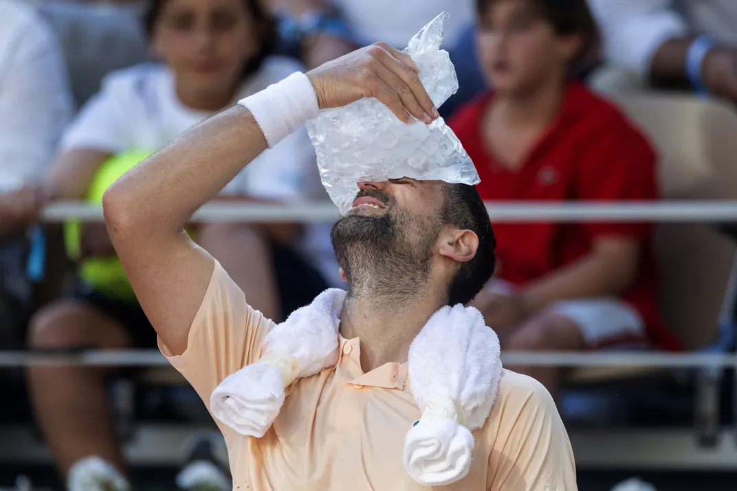 a tennis player leans his head back and holds a bag of ice to his forehead