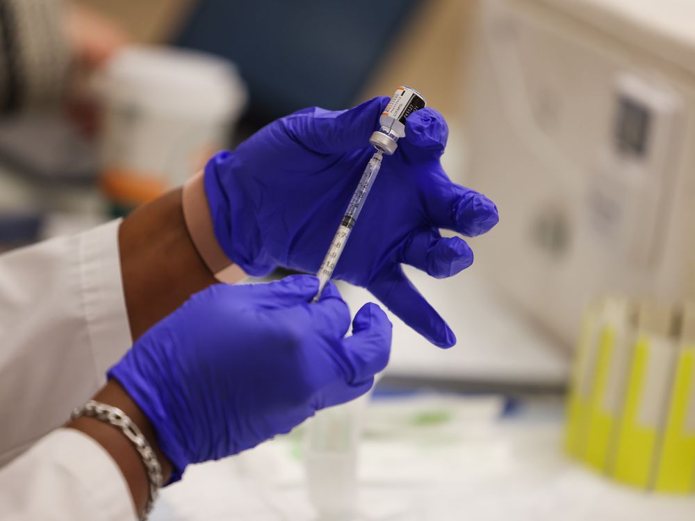 A close-up of gloved hands filling a syringe with a Covid-19 booster shot