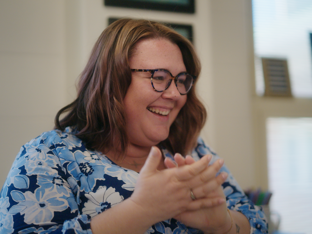 Teacher with short brown hair and glasses, wearing a blue shirt is smiling and clapping