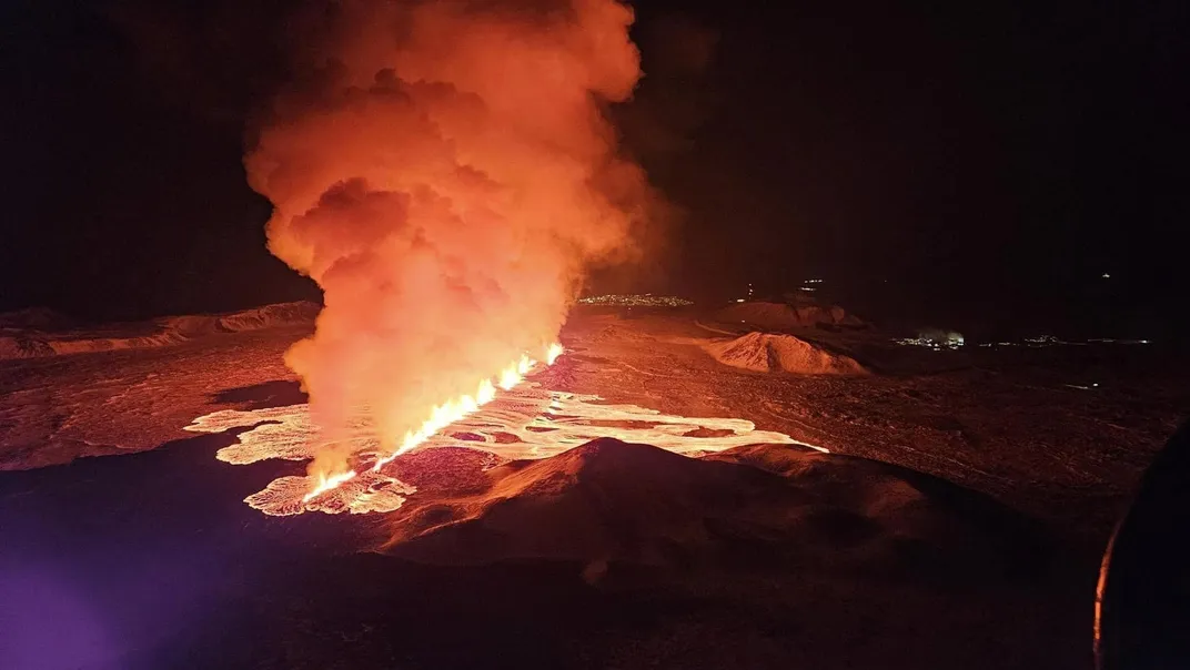 Lava flows and smoke billows from a fissure in the ground in the dark